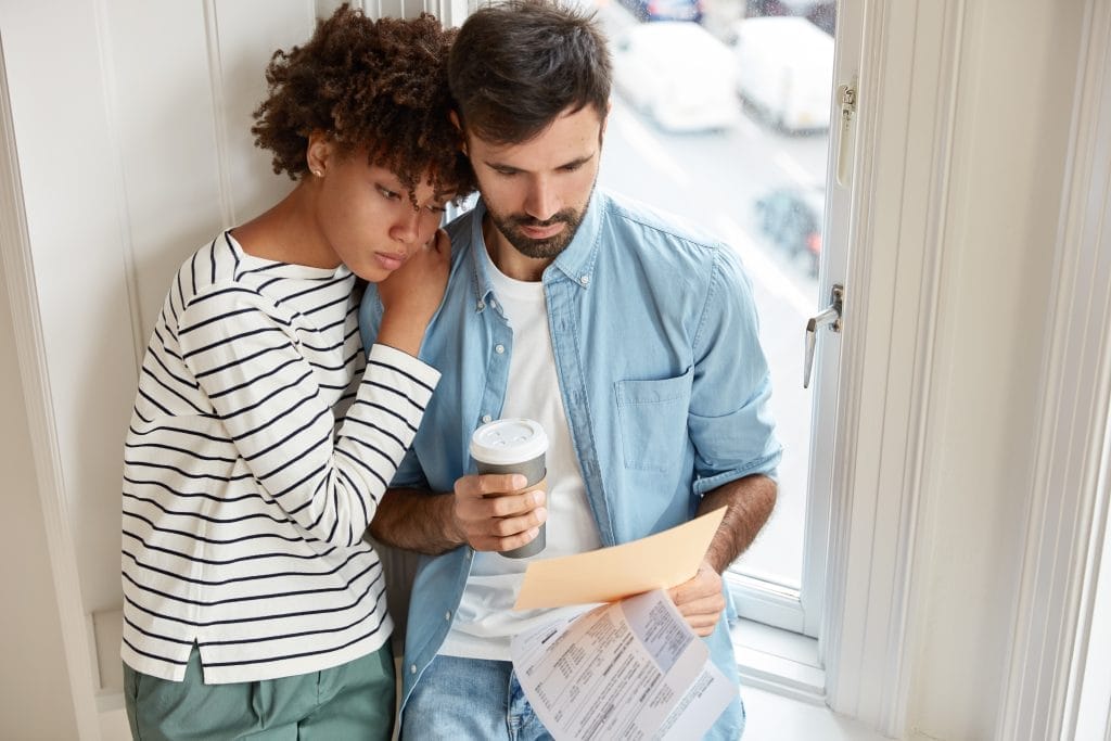 Diverse partners have business connections, direct contact work together at domestic atmosphere. Serious black female model leans at shoulder of husband, stand near window sill, control sales