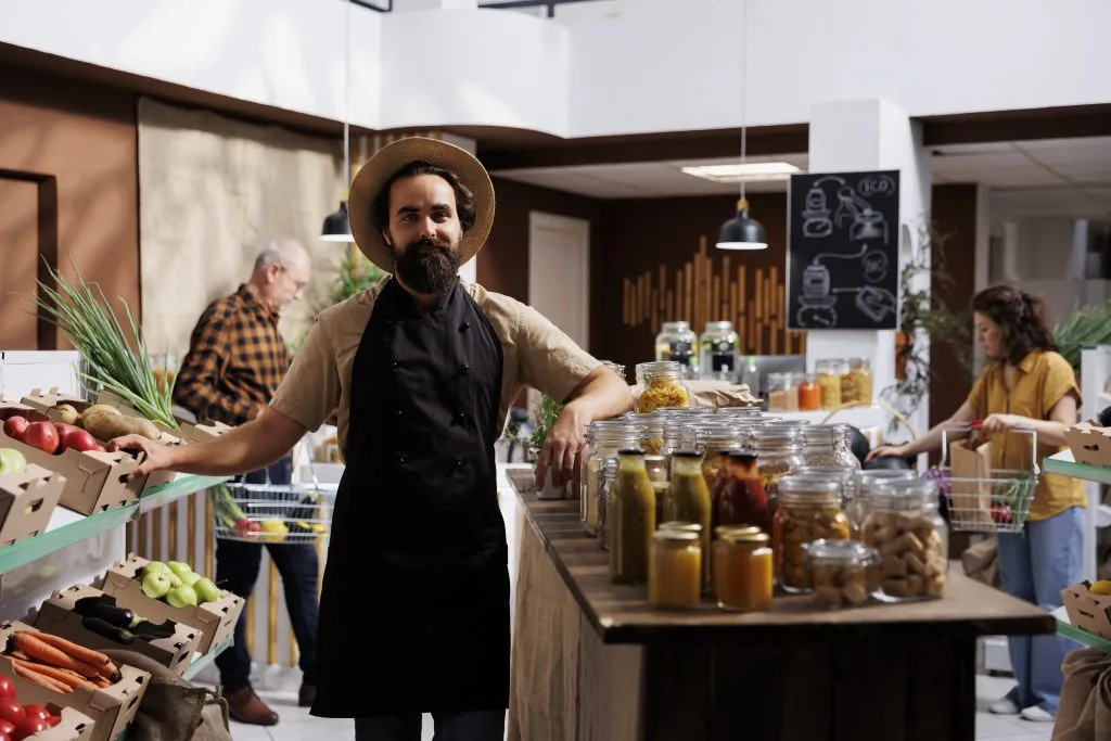 Portrait of smiling zero waste shop storekeeper holding organic bio vegetables in shopping basket. Happy seller working in chemicals free healthy groceries local neighborhood store